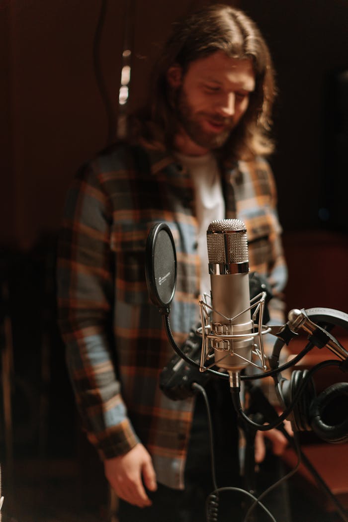 Male musician in recording studio with condenser microphone, captured in a warm, moody atmosphere.