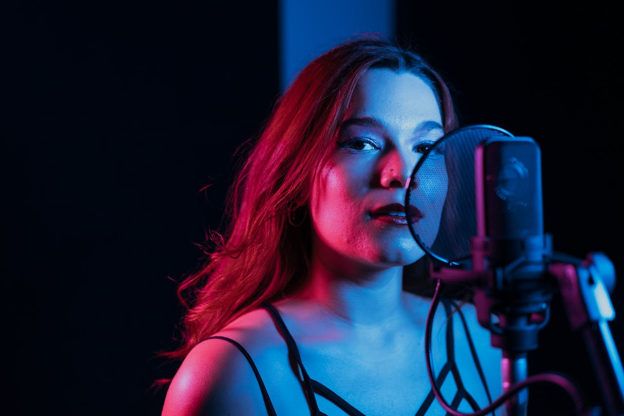 A woman singing into a microphone in a creatively lit studio setting.