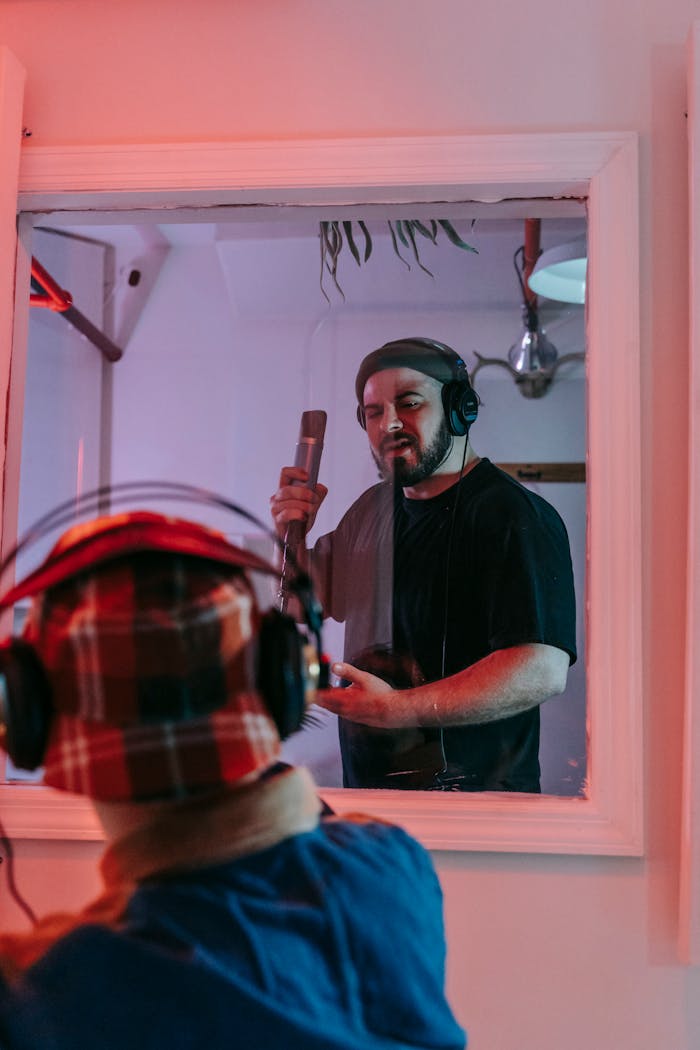 Bearded man singing into a microphone in a professional music studio.